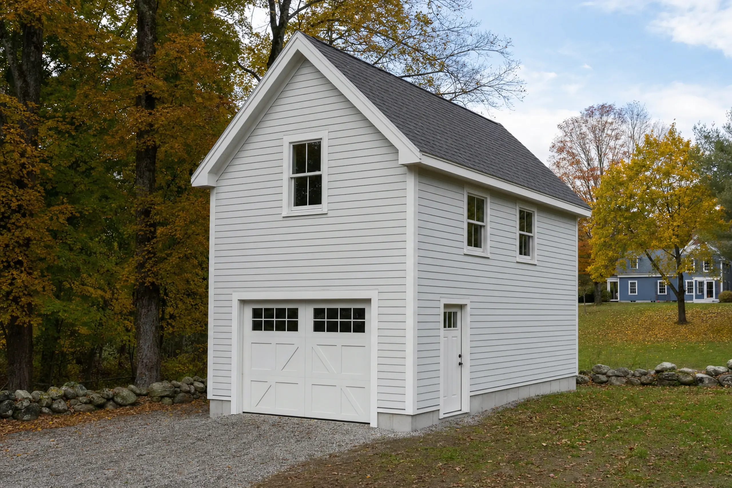 White two-story building with garage door and side door, surrounded by autumn trees and grass.