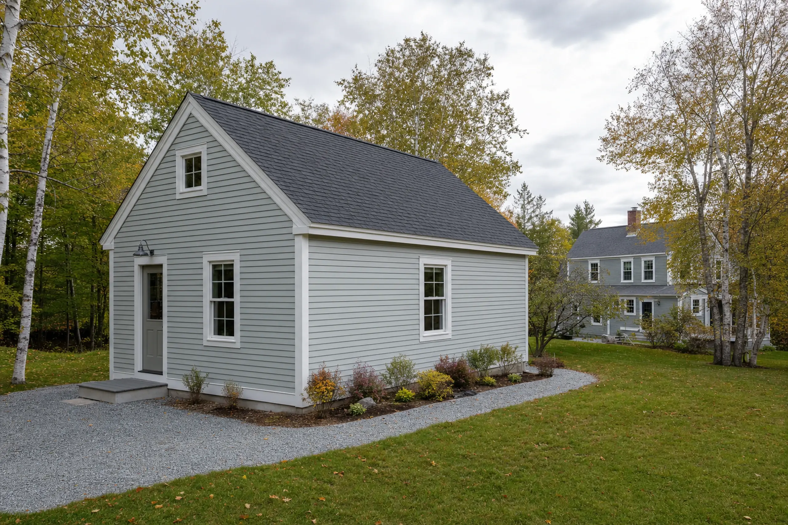 Small gray house with white trim and dark roof in a grassy yard with trees.