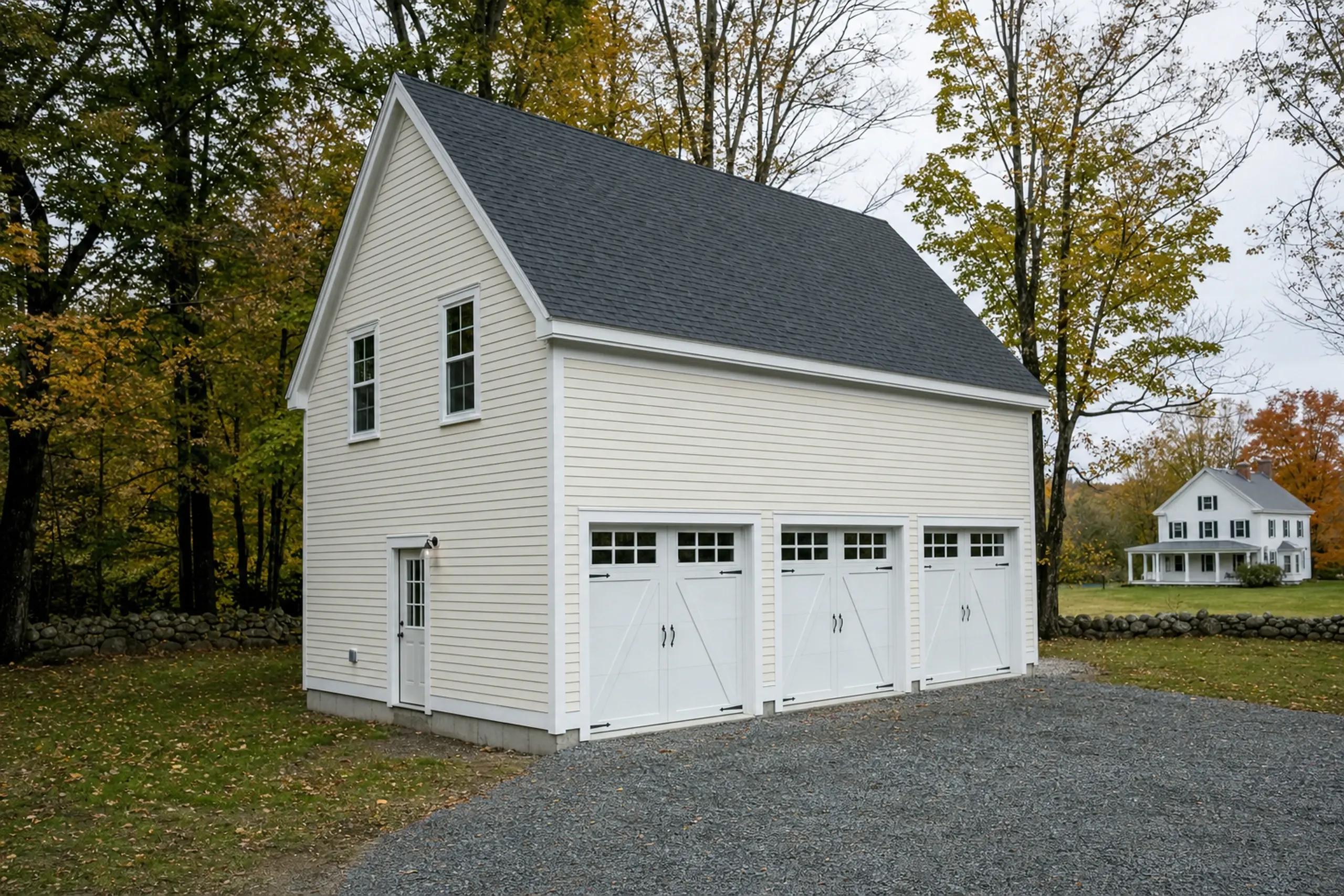 Cream-colored two-story garage with three white doors and a gray roof in a wooded setting.