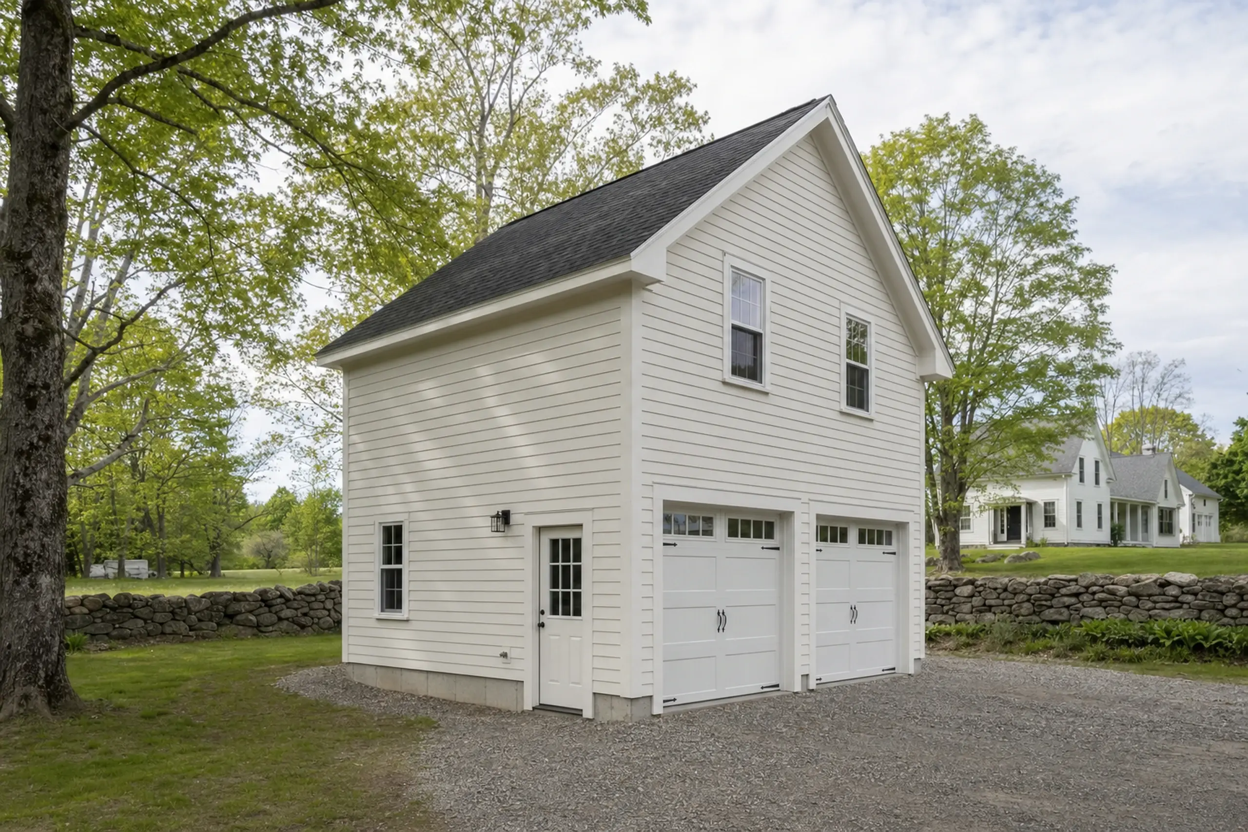White two-story building with black roof, two garage doors, and a side door in a green yard.