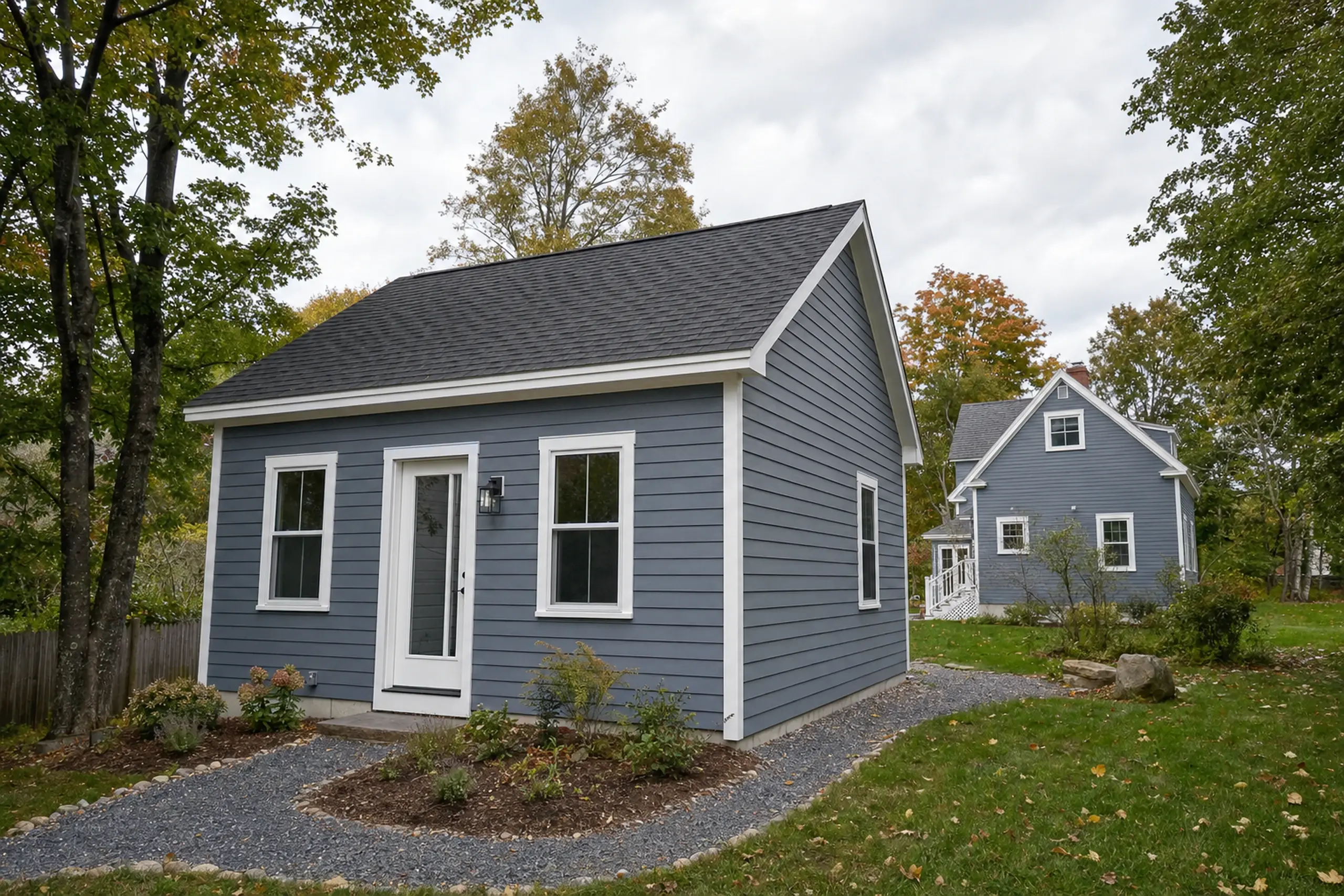 Two blue houses with white trim in a green yard with trees and gravel paths.