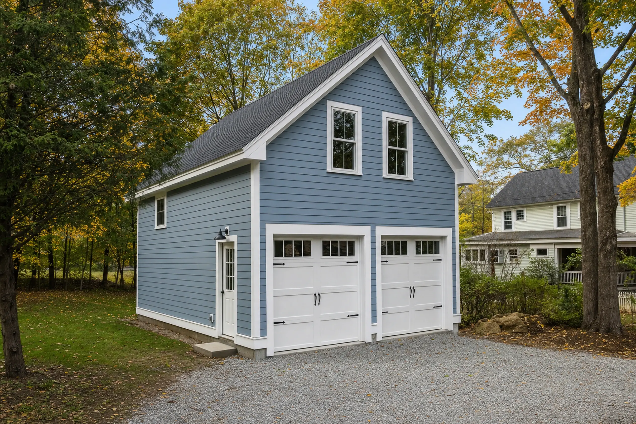 Blue two-car garage with white trim in a leafy suburban setting during autumn.