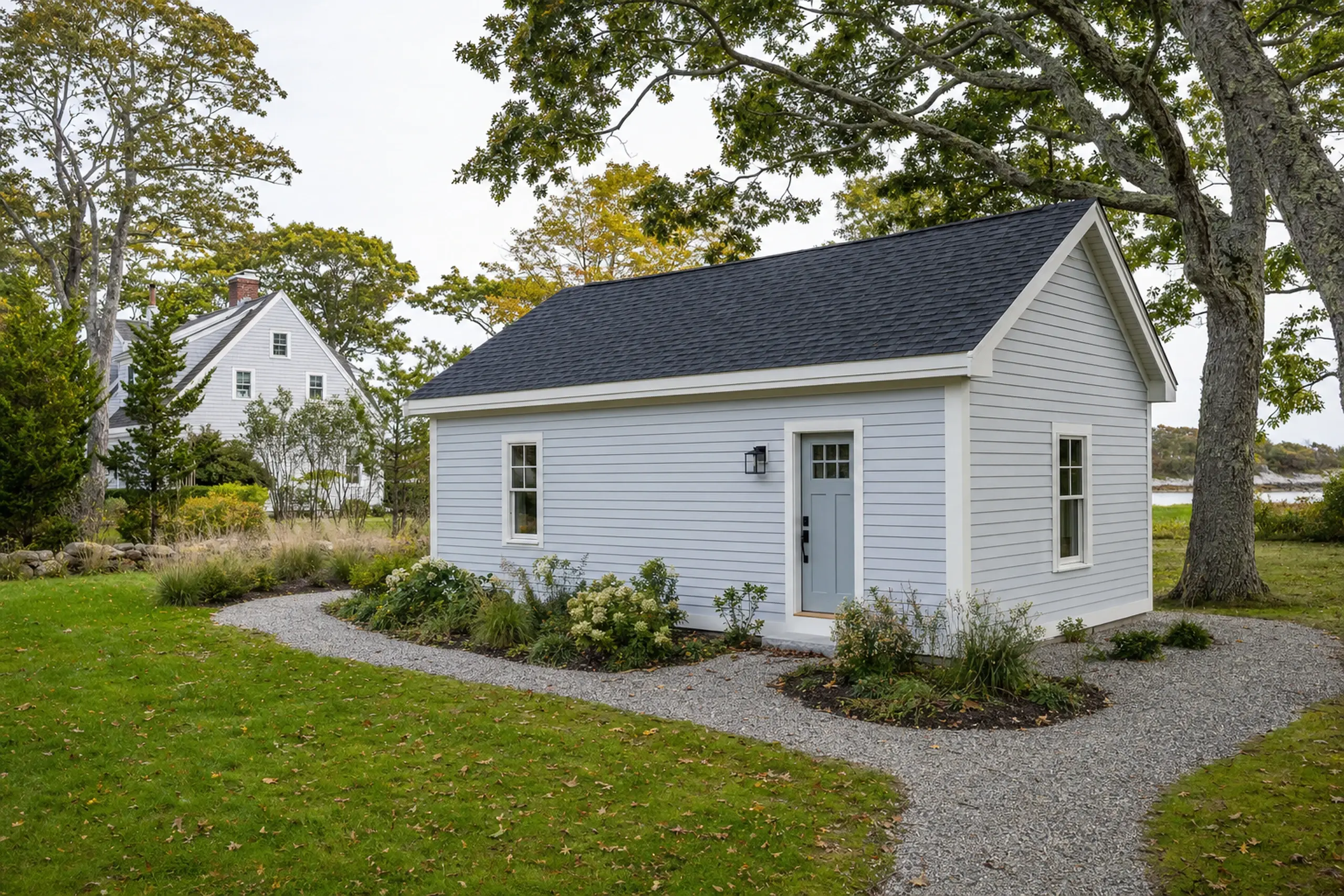 Small light gray building with dark roof, white trim, surrounded by grass and trees.