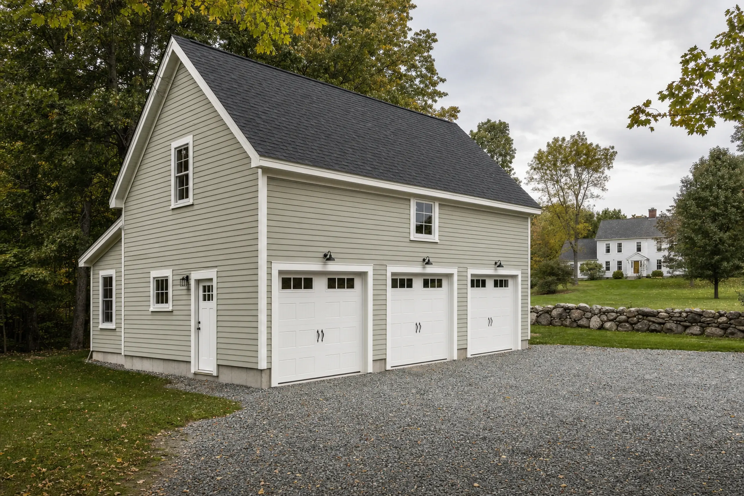 Light gray garage with three white doors and a black roof in a green, wooded setting.