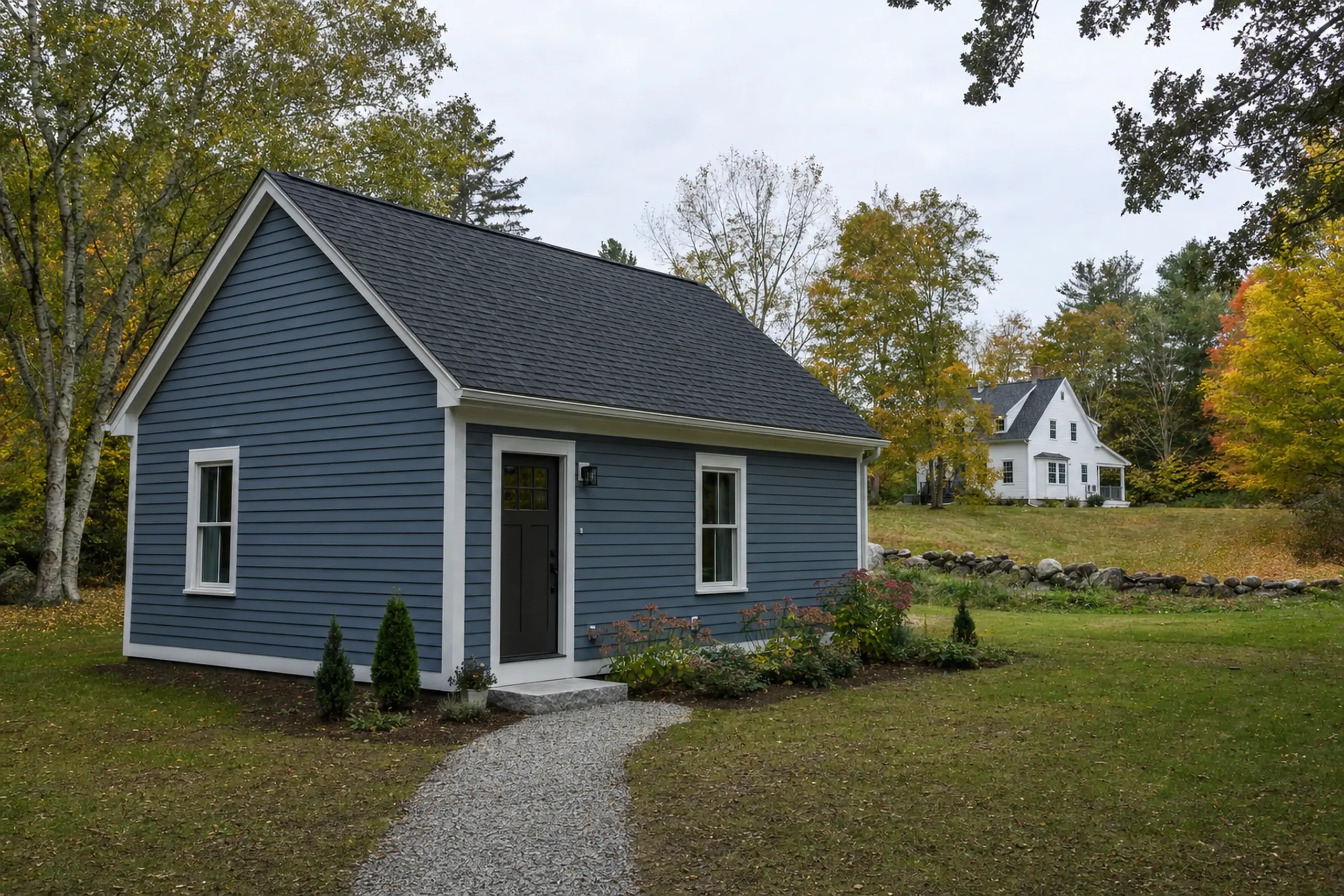 Blue single-story house with white trim in a grassy yard with trees and a gravel path.